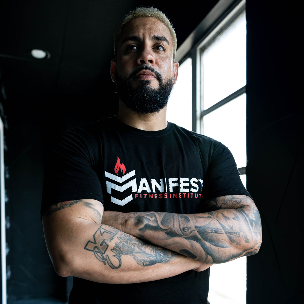 Manifest Fitness Apparel — model wearing the Manifest tee in low gym light