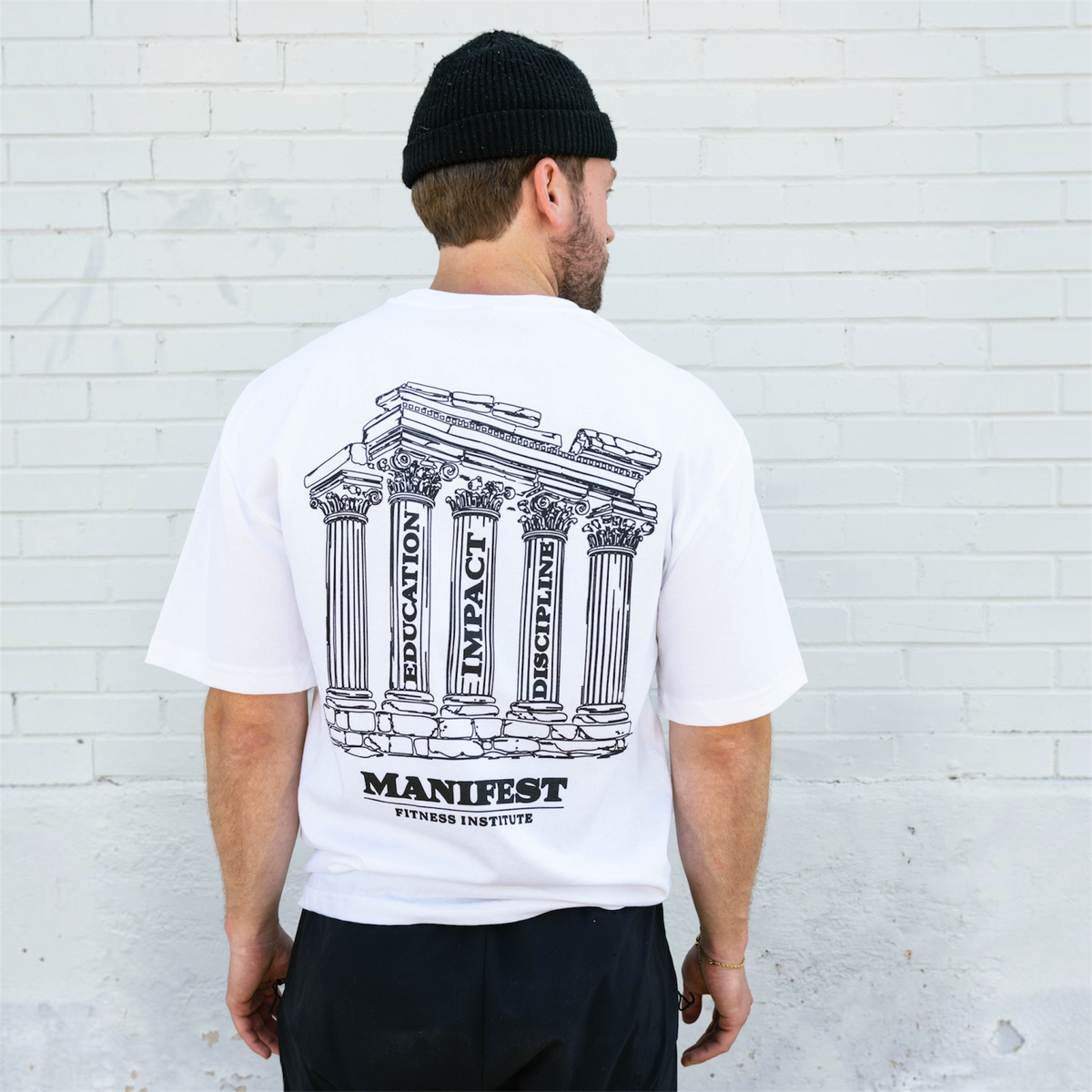 Model wearing the white Colosseum Tee, showing the pillar graphic across the back